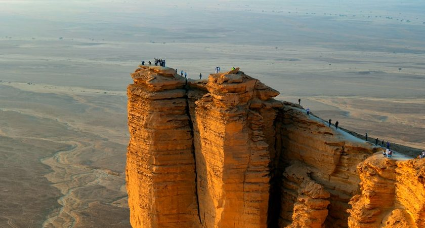 Tourists standing at the Edge of the World cliff, overlooking a vast desert landscape near Riyadh, Saudi Arabia - (Credits zamzam.com)