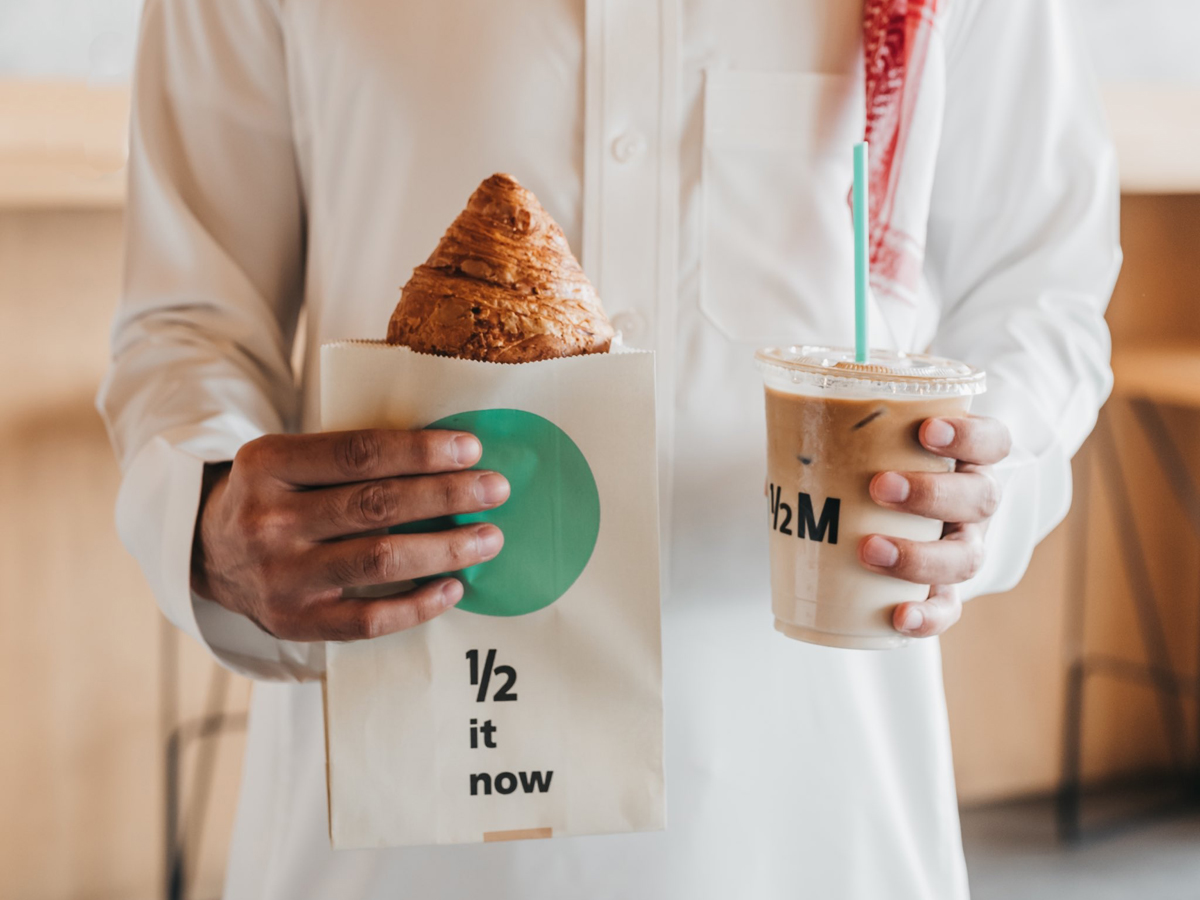 A Saudi man holding a croissant and coffee - (Credits Time Out Riyadh)