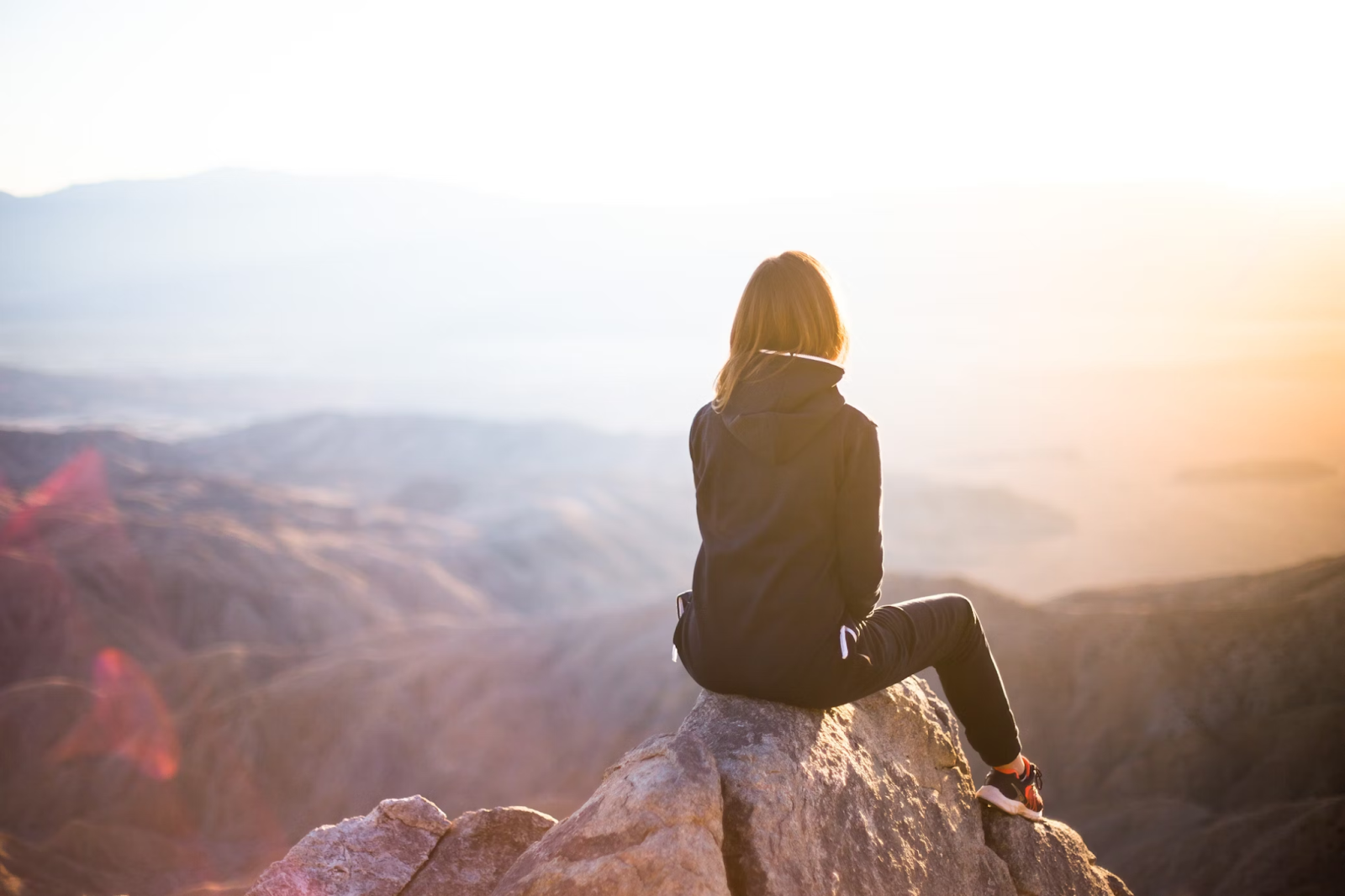 A solo female traveler sitting on the edge of a mountain - (Credits Unsplash)