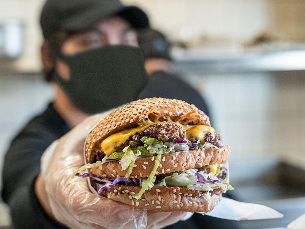 A server holding a double-patty beef burger - (Credits Section B)